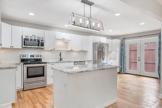 kitchen featuring stainless steel appliances, white cabinetry, light wood-type flooring, a center island, and decorative light fixtures