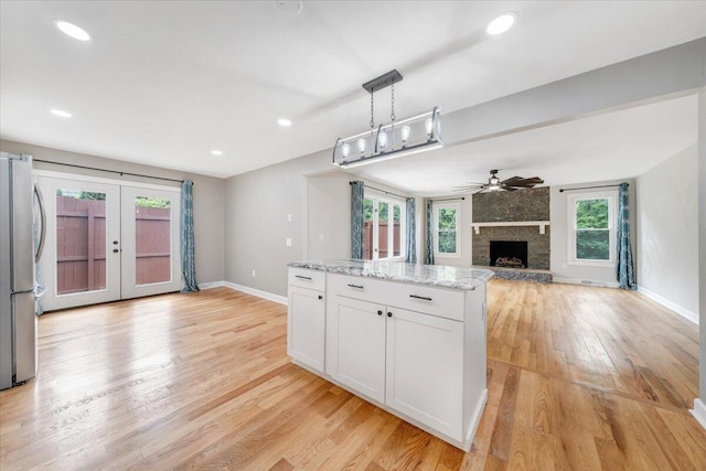 kitchen with white cabinets, light stone counters, open floor plan, freestanding refrigerator, and hanging light fixtures