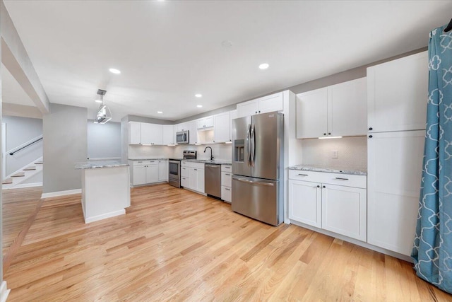 kitchen with light stone counters, appliances with stainless steel finishes, white cabinetry, a sink, and light wood-type flooring