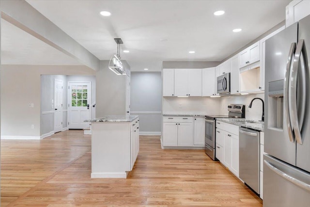 kitchen featuring light stone counters, stainless steel appliances, hanging light fixtures, white cabinets, and a sink