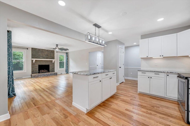 kitchen with white cabinets, open floor plan, light stone countertops, stainless steel range with electric stovetop, and pendant lighting