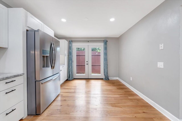 kitchen with french doors, light wood-style flooring, white cabinets, stainless steel fridge, and baseboards