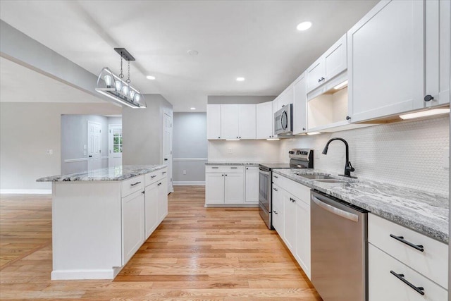 kitchen featuring light stone counters, decorative light fixtures, stainless steel appliances, white cabinetry, and a sink