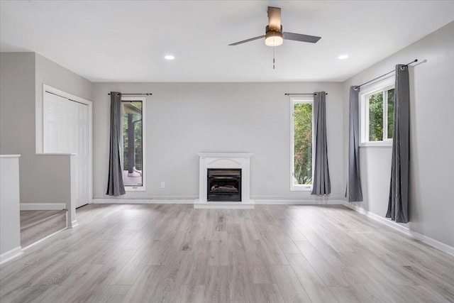 unfurnished living room with a fireplace with raised hearth, recessed lighting, light wood-type flooring, and baseboards