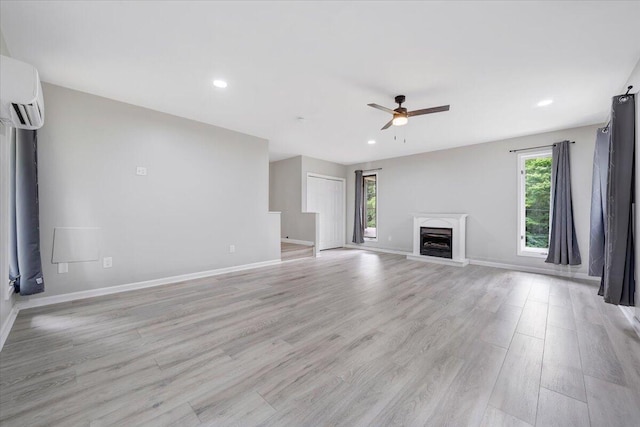 unfurnished living room with a fireplace with raised hearth, a ceiling fan, baseboards, light wood-type flooring, and a wall mounted air conditioner