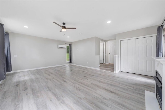 unfurnished living room featuring light wood finished floors, baseboards, a wall unit AC, ceiling fan, and recessed lighting