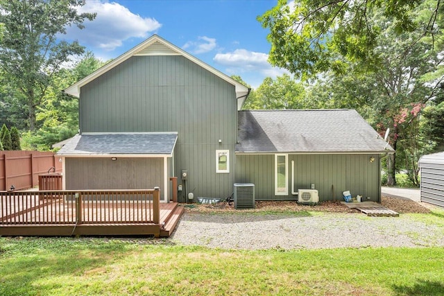 back of house featuring a shingled roof, a lawn, fence, a wooden deck, and central AC