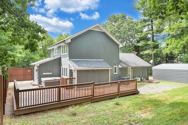 back of property with a hot tub, a lawn, roof with shingles, fence, and a wooden deck