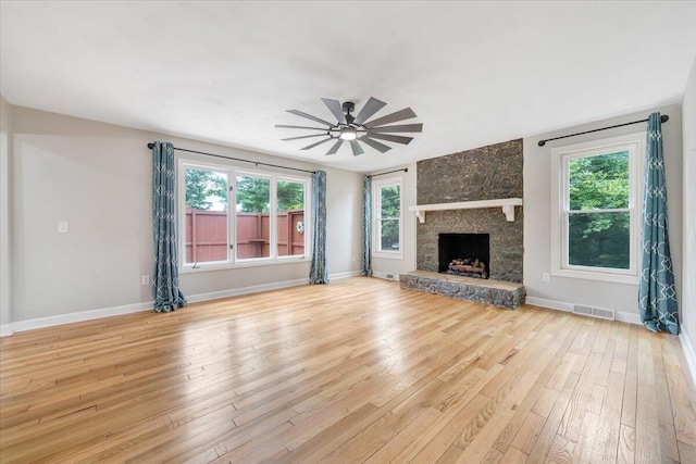 unfurnished living room featuring a stone fireplace, light wood-style flooring, plenty of natural light, and visible vents