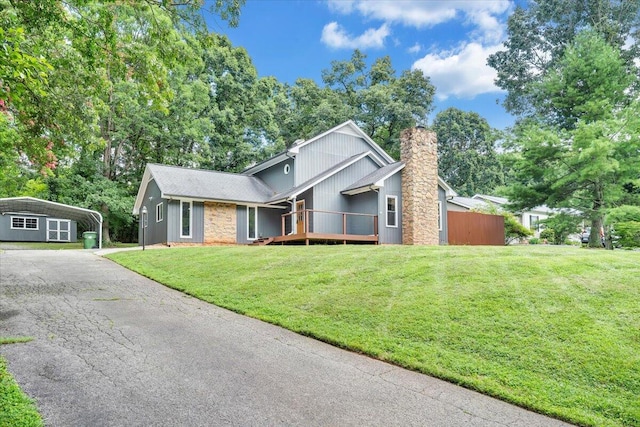 view of front facade featuring aphalt driveway, a chimney, a detached carport, a front lawn, and a wooden deck