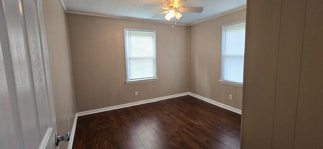 empty room featuring crown molding, a healthy amount of sunlight, ceiling fan, and dark hardwood / wood-style floors