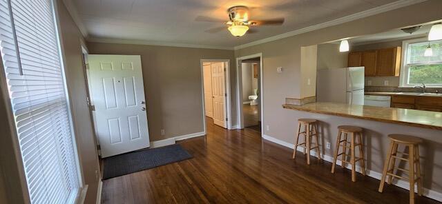 kitchen featuring ornamental molding, white appliances, ceiling fan, a breakfast bar, and dark wood-type flooring