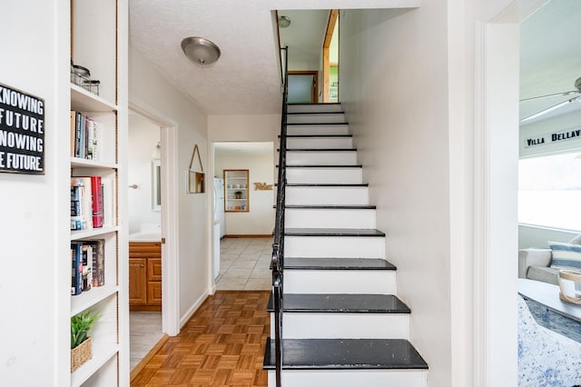 stairway with parquet flooring, ceiling fan, and a textured ceiling