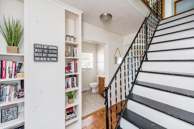 stairway featuring a textured ceiling and parquet flooring