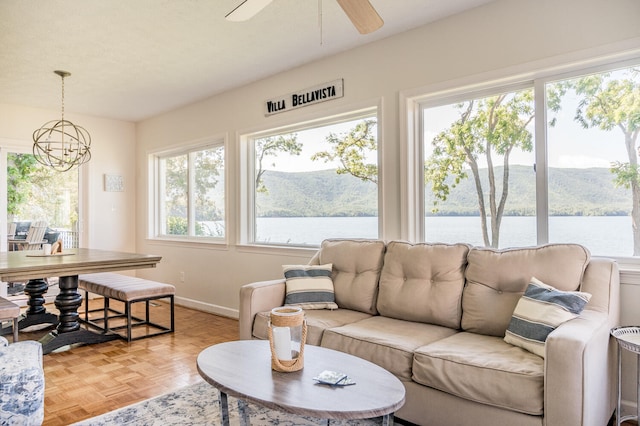 living room with light parquet floors, a water and mountain view, and ceiling fan with notable chandelier