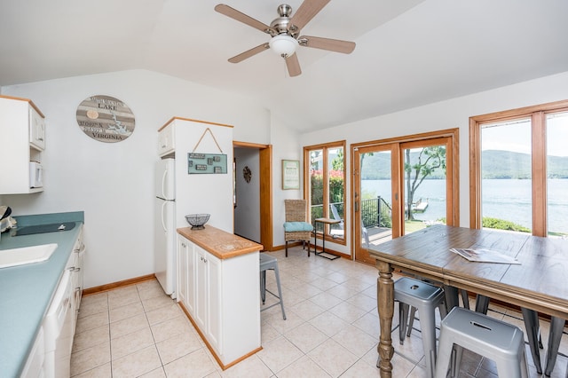 kitchen with a water and mountain view, white cabinets, lofted ceiling, and light tile floors