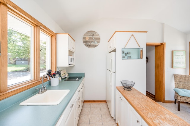 kitchen featuring white appliances, vaulted ceiling, light tile floors, sink, and white cabinetry