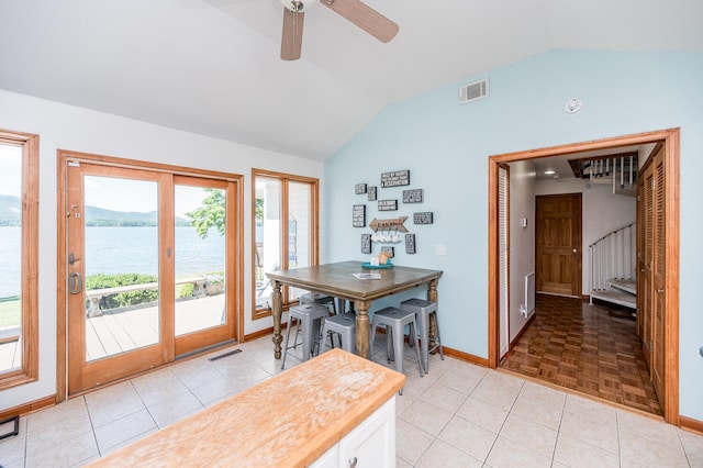 dining space with vaulted ceiling, a water view, and light tile floors