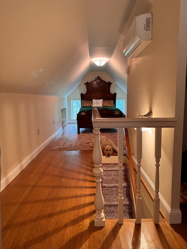 additional living space featuring vaulted ceiling, a wall mounted air conditioner, and hardwood / wood-style flooring