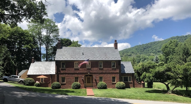 colonial inspired home with a mountain view and a front lawn