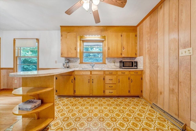 kitchen featuring sink, wood walls, kitchen peninsula, ceiling fan, and a baseboard heating unit