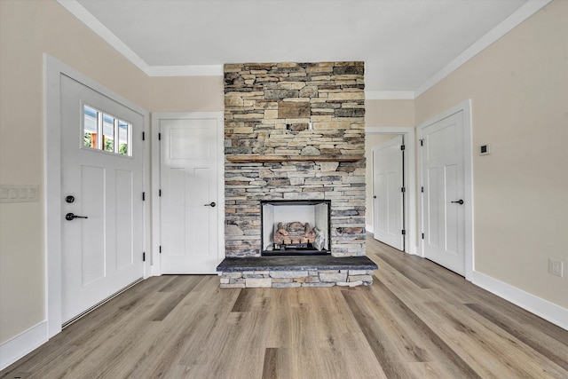 foyer featuring a stone fireplace, light hardwood / wood-style floors, and ornamental molding