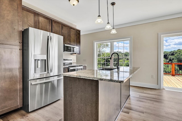 kitchen with light stone countertops, sink, stainless steel appliances, an island with sink, and dark brown cabinets