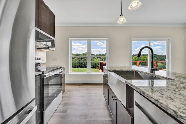 kitchen with dark brown cabinetry, hanging light fixtures, stainless steel appliances, light stone counters, and light wood-type flooring