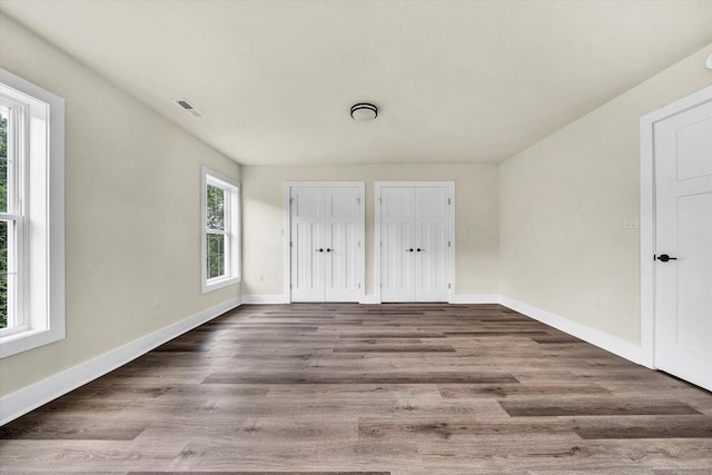 unfurnished bedroom featuring hardwood / wood-style floors and multiple closets