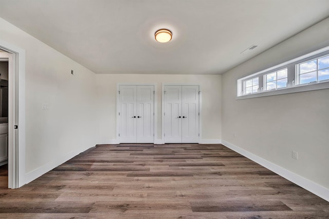 unfurnished bedroom with dark hardwood / wood-style flooring and two closets