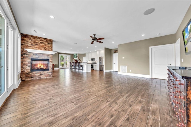 unfurnished living room featuring ceiling fan, brick wall, hardwood / wood-style floors, and a brick fireplace