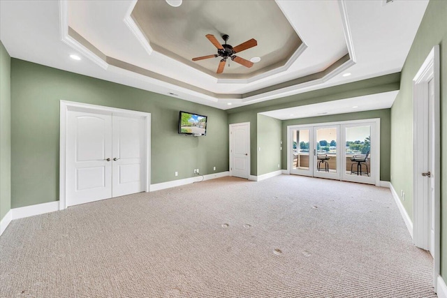 unfurnished bedroom with a raised ceiling, light colored carpet, access to exterior, and ceiling fan