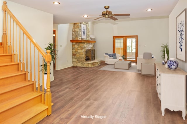 living room featuring light wood-type flooring, a stone fireplace, recessed lighting, and stairs