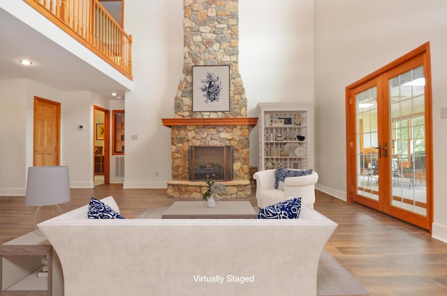 living area featuring french doors, a fireplace, a towering ceiling, wood finished floors, and baseboards