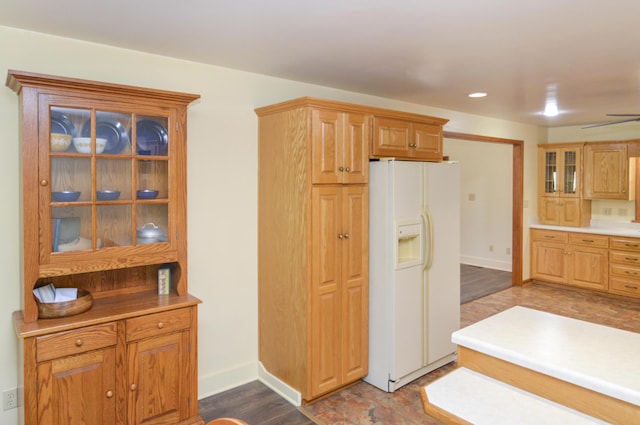 kitchen featuring white refrigerator with ice dispenser, dark wood-type flooring, baseboards, light countertops, and glass insert cabinets