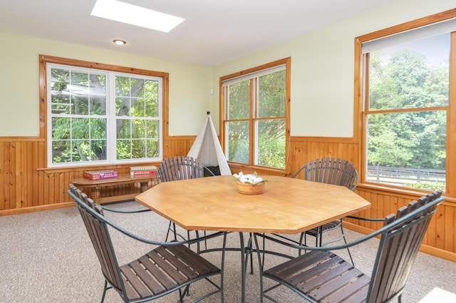 dining room with a skylight, a wainscoted wall, and wooden walls