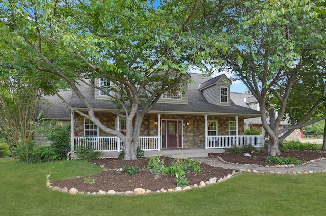 new england style home featuring a porch, a front yard, stone siding, and roof with shingles