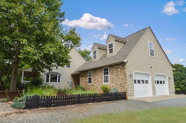 view of front of home with stone siding, roof with shingles, fence, and driveway