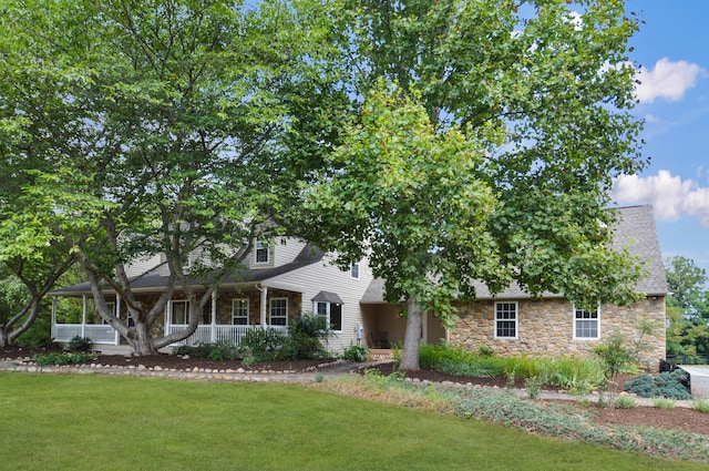 view of front of home with stone siding, a front lawn, roof with shingles, and a porch