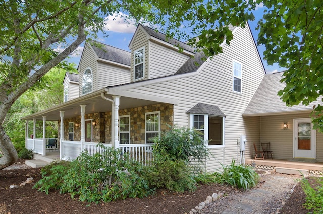 view of front of property featuring a porch, stone siding, and a shingled roof