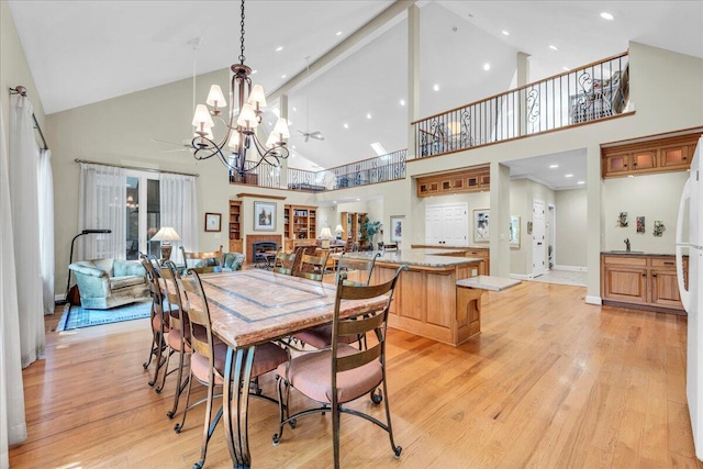 dining room featuring ceiling fan with notable chandelier, light wood-type flooring, beam ceiling, and high vaulted ceiling