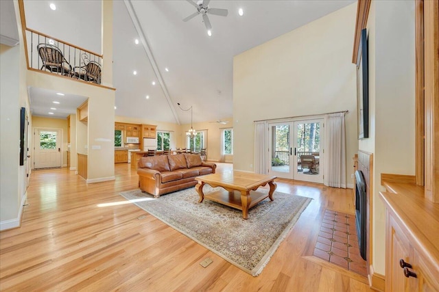 living room with french doors, ceiling fan with notable chandelier, light hardwood / wood-style flooring, and high vaulted ceiling