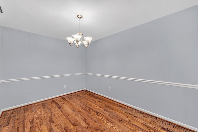 spare room with an inviting chandelier and wood-type flooring