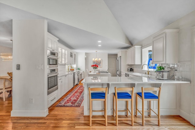 kitchen featuring a breakfast bar, white cabinets, vaulted ceiling, light hardwood / wood-style floors, and kitchen peninsula