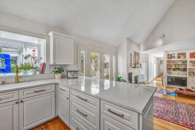 kitchen with a brick fireplace, light hardwood / wood-style flooring, kitchen peninsula, lofted ceiling, and white cabinets