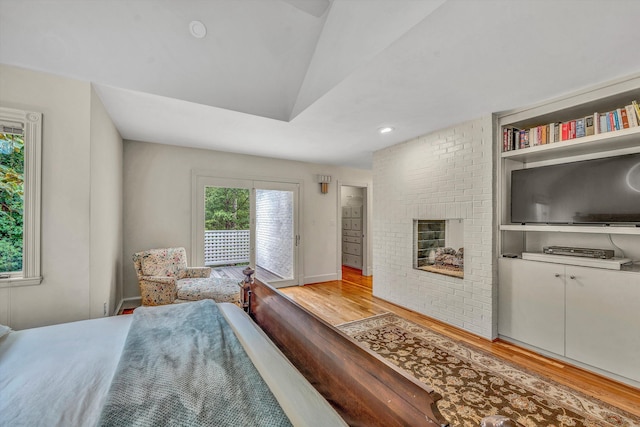 bedroom with a brick fireplace, lofted ceiling, and light hardwood / wood-style flooring