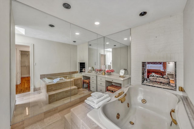 bathroom with a multi sided fireplace, vanity, and a relaxing tiled tub