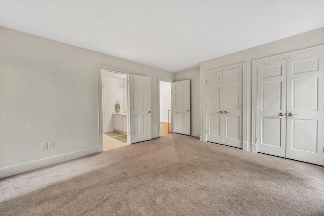 unfurnished bedroom featuring ensuite bath, multiple closets, and light carpet