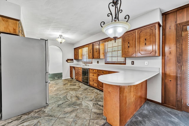 kitchen featuring beverage cooler, arched walkways, brown cabinetry, freestanding refrigerator, and a peninsula