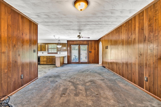 unfurnished living room with arched walkways, light colored carpet, wood walls, ceiling fan, and baseboards